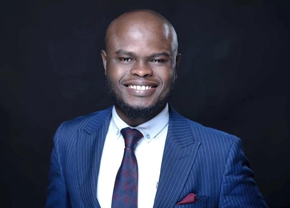 Professional portrait of Adeola Oladimeji, smiling with a blue suit and tie.